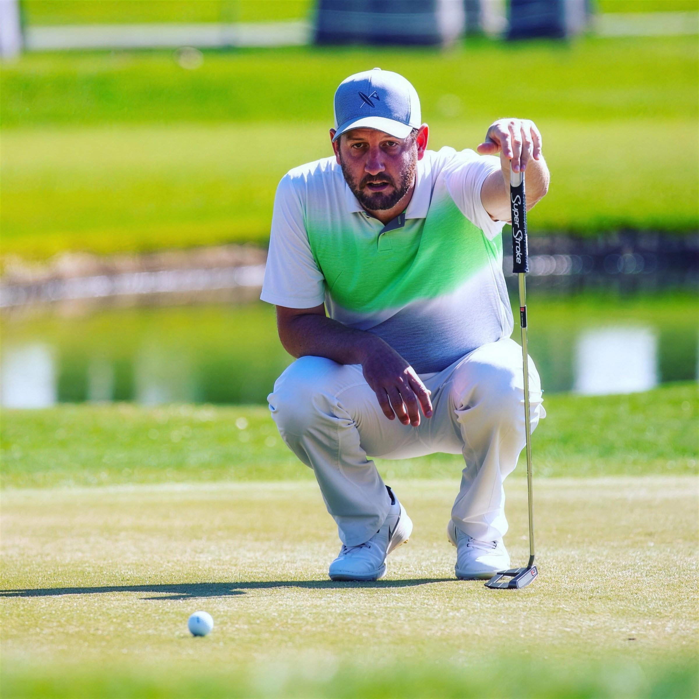 Tyler Ostrovsky crouched on a green, reading a putt